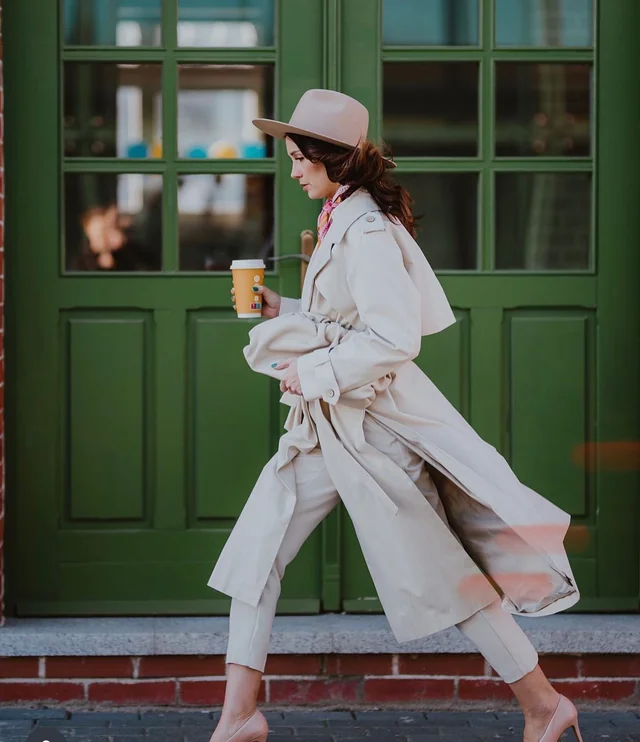 The Lisbon trench, walking with coffee and a fedora beside green cafe windows
